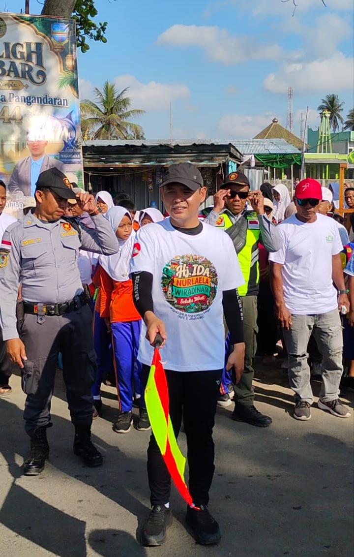 Kepala Desa Pangandaran, Adi Fitriadi, S.HP., memegang bendera saat mengikuti jalan sehat dalam rangkaian Milangkala ke-44 Desa Pangandaran di kawasan Pantai Timur Pangandaran, Senin (21/9/2026). Foto : Agit/ Inakor
